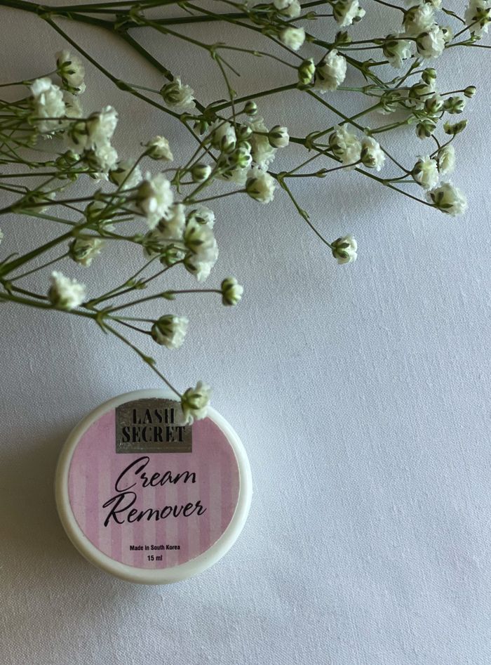 Elegant Lash Secret cream remover placed with delicate white flowers on a clean surface.